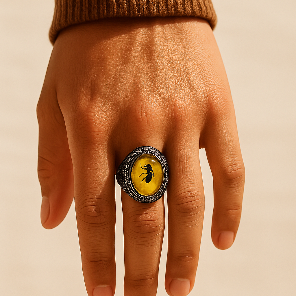 Hand wearing a ring with a yellow stone and black insect design on a beige background